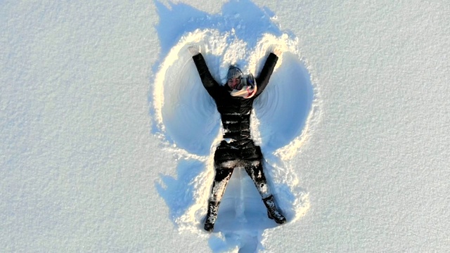 顶部鸟瞰图的年轻快乐微笑的女孩使手臂雪天使的形象和躺在雪，冬季户外活动视频素材