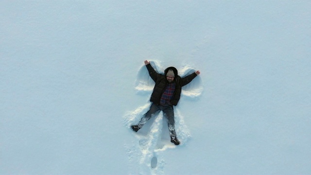 顶部鸟瞰图的快乐微笑的人制造雪天使的手臂和躺在雪，复制空间。冬季户外活动概念视频素材