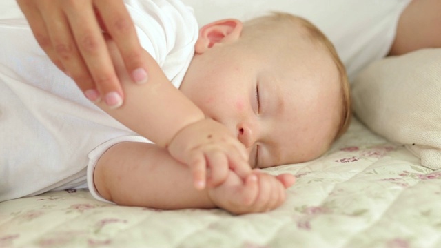 新生儿在床上睡觉的肖像。妈妈轻轻地抚摸着宝宝的手。视频素材