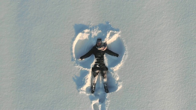 顶部鸟瞰图的年轻快乐微笑的女孩使手臂雪天使的形象和躺在雪，冬季户外活动视频素材