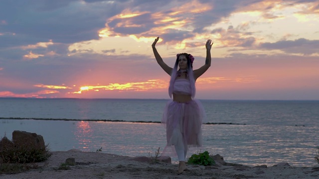 漂亮的女人，浓妆艳抹，穿着粉红色的裙子，在河岸上跳舞。一个性感的女孩的舞蹈与一个美妙的发型与鲜花。缓慢的运动。视频下载
