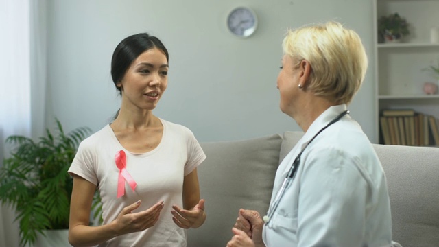 女志愿者戴着粉红丝带与医生交谈，在诊所里提供信息视频下载