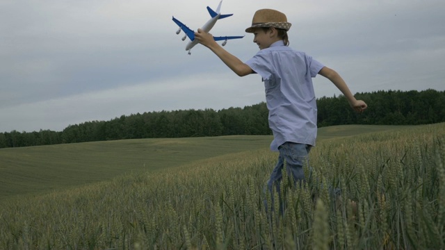 戴着草帽的快乐男孩梦想家手里拿着一架飞机跑过田野视频素材
