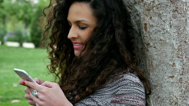 一个年轻漂亮的女人在公园里用智能手机的慢镜头视频素材