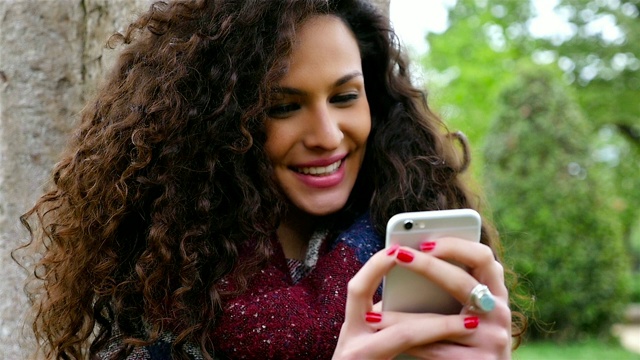 一个年轻漂亮的女人在公园里用智能手机的慢镜头视频素材