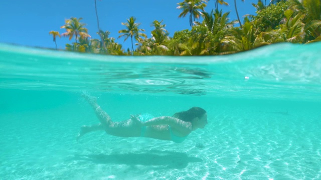一半一半:年轻女子在异国海岛度假期间在水下游泳。视频下载