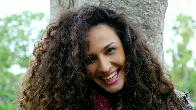 一个快乐的年轻女子的肖像美丽的卷发微笑在一个公园，慢镜头视频素材