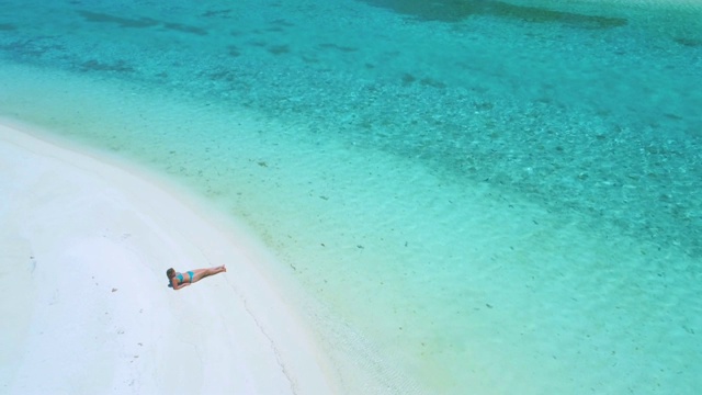 一名年轻女子躺在沙滩上，在碧绿的大海边晒太阳。视频下载