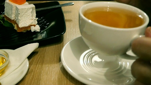 女人在咖啡馆或餐馆吃蛋糕，用勺子拿起它，然后从杯子里喝茶。视频素材
