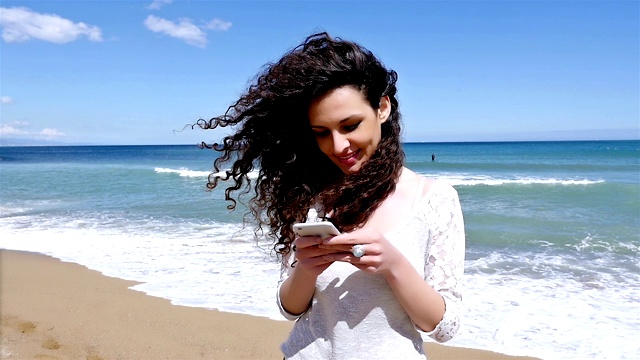 一个年轻漂亮的女人在海滩上用智能手机自拍，慢镜头视频素材