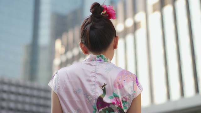 穿着粉红色旗袍的中国妇女，微笑着拿着扇子。视频下载
