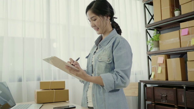 聪明的亚洲商界女性企业主中小企业网上使用电话接收客户检查产品在股票和写在剪贴板在家里工作。小企业主在家办公的概念。视频素材