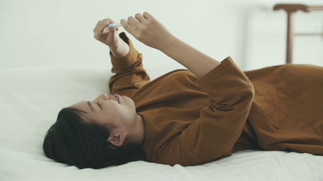 亚洲妇女躺在床上，并持有阳性怀孕测试试剂盒视频素材