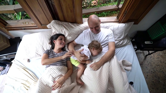父母与可爱的女儿在床上玩得开心视频素材