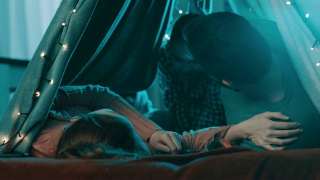 一对浪漫的夫妇躺在家里的帐篷里，他们的女儿向他们走来视频下载