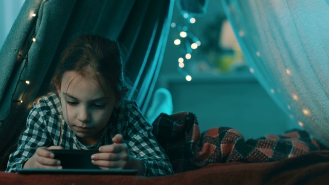 快乐的小女孩在家里的帐篷里用智能手机微笑视频下载