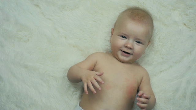 5个月大的小男孩躺在毯子上，慢镜头中他对着镜头微笑。视频下载