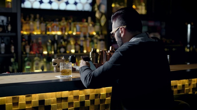一个男人静静地坐在酒吧里，端着一杯威士忌，在网上聊天视频下载