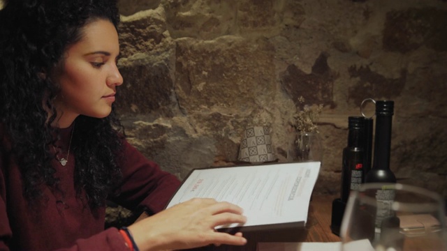 西班牙裔年轻女子阅读菜单，并订购准备在餐厅用餐视频下载