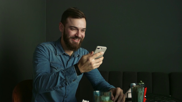 咖啡厅里一个留着胡子的年轻人的肖像。蓝衬衫男使用视频通话视频素材