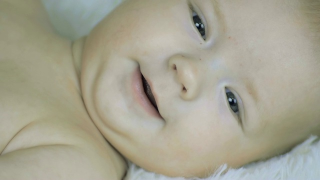 一个六个月大的男孩赤裸着躺在白毯子上的特写视频素材