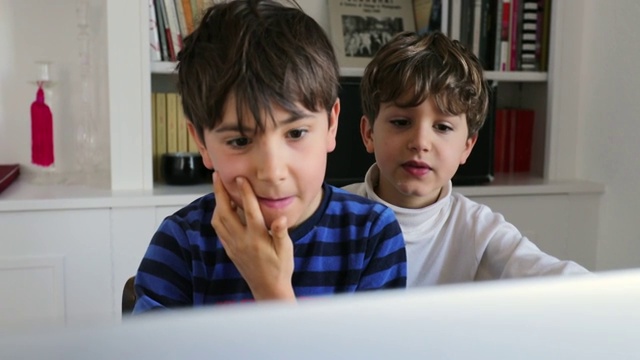 孩子们早上坐在电脑屏幕前。孩子们上网在网上寻找媒体视频素材