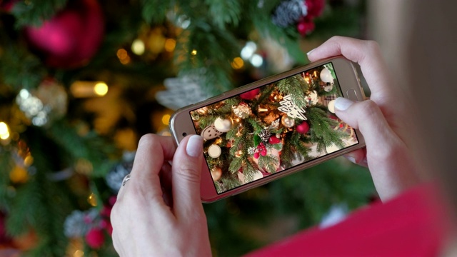 美丽的女人在家里用智能手机拍摄圣诞树和新年礼物。圣诞、寒假与人观念。第一个人开枪。视频下载