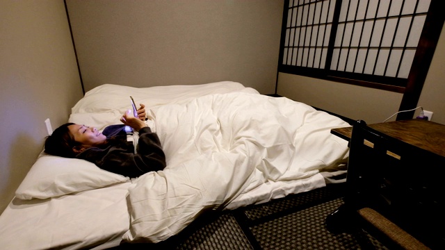 4K拍摄:一名亚洲女性住在日式传统酒店。她在深夜睡觉前和朋友们用手机聊天视频素材
