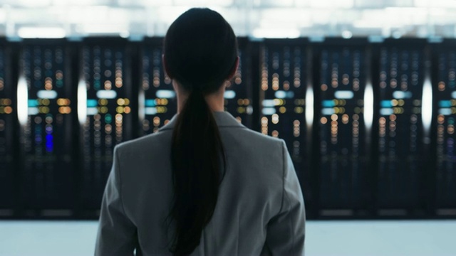 一位身穿夹克的女IT总工程师走向数据中心机房的服务器机架。视频下载