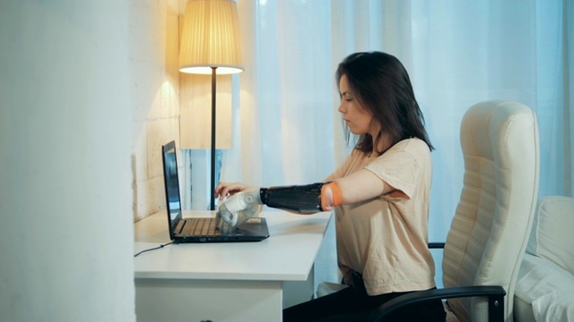 一位女士正在用她的机械手在笔记本电脑上工作，喝着咖啡视频素材