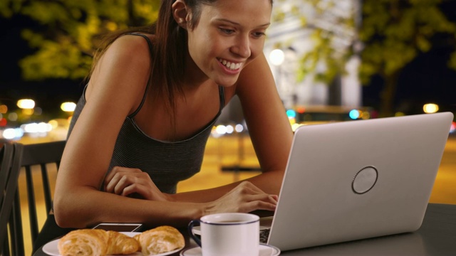 白种女人晚上在外面喝着咖啡在笔记本电脑上浏览视频素材