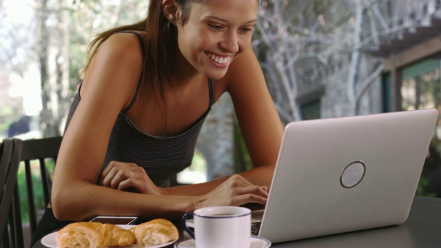 快乐的女人在后院用笔记本电脑吃早餐视频素材