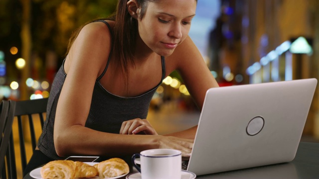 巴黎的一名年轻女子坐在外面用着笔记本电脑吃着羊角面包视频素材