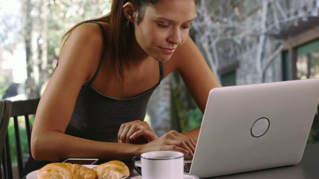 年轻女子坐在后院吃早餐，用笔记本电脑视频素材