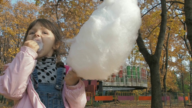 温暖阳光明媚的秋日，小女孩在游乐园吃棉花糖。视频素材