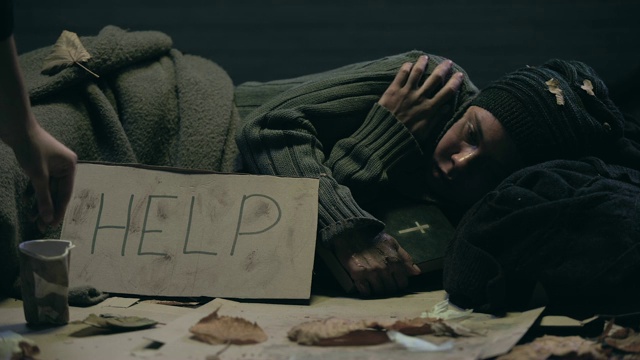 乞丐躺在街上拿着圣经，在纸板上写着帮助字，请求施舍视频下载