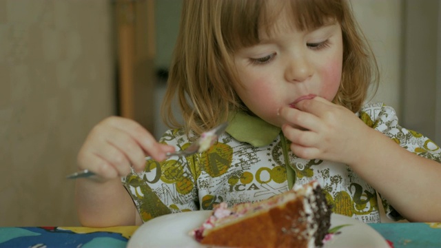 可爱的小男孩吃着新鲜甜蜜的巧克力蛋糕。特写镜头。迷人的小男孩，大大的眼睛里充满了爱和鲜奶油，用手指舔奶油，然后用涂满奶油的手指坐在桌前吃视频素材