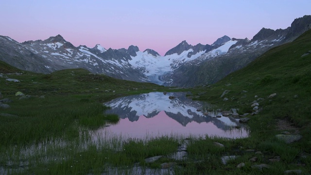 冰雪覆盖的奥伯拉霍恩山和他的冰川反射在格里姆塞尔山口的湖泊，日出的黄昏。格里姆塞尔隘口是大陆的分水岭。视频下载