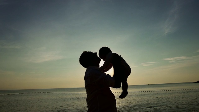 家庭在海滩概念，白人父亲玩和抱着他的儿子在热带海滩上的日落。视频素材
