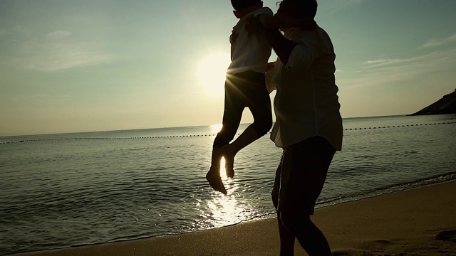 日出时父亲和儿子在海滩上击掌，他们一起度过了宝贵的家庭时光。视频素材