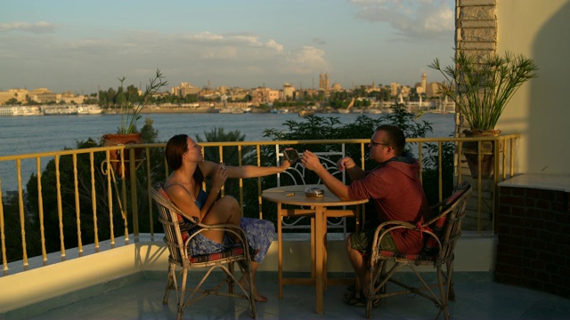 一男一女正坐在俯瞰河流的露台上的一张桌子旁。视频下载