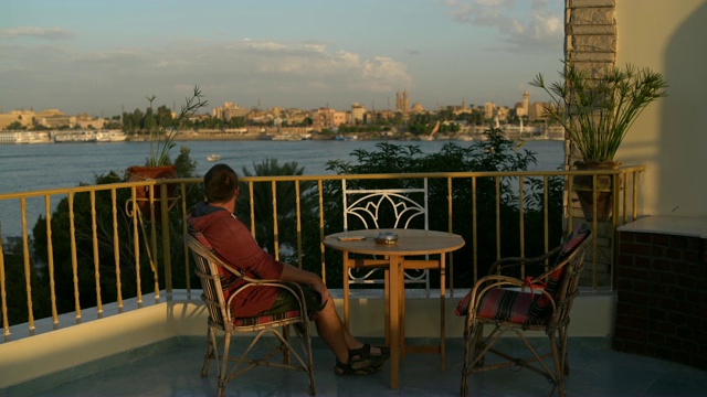 一个男人坐在露台上，眺望着河，欣赏着风景。视频下载