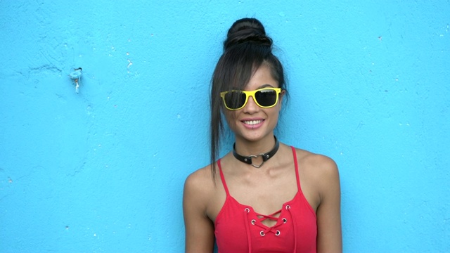 4K年轻女子戴着太阳镜站在蓝色墙壁前视频下载