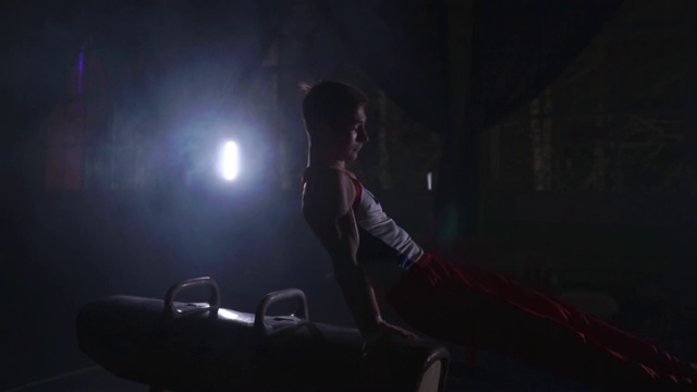 男子体操运动员在鞍马上表演奥运项目的动作，在慢动作中表演旋转和翻滚，在黑暗的房间里围绕着烟雾和柜台灯努力训练，为奥运会做准备视频素材