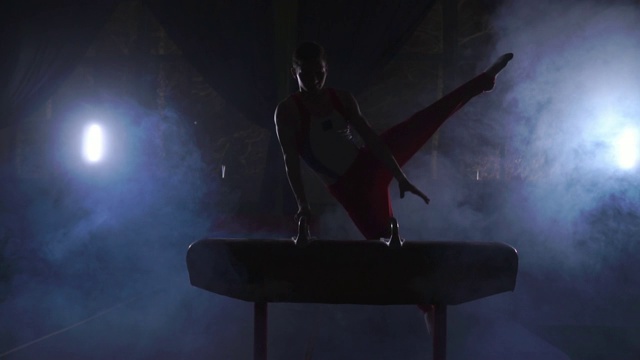 男子体操运动员在烟雾缭绕的暗室中慢动作表演鞍马。运动是为了健康和成就视频素材