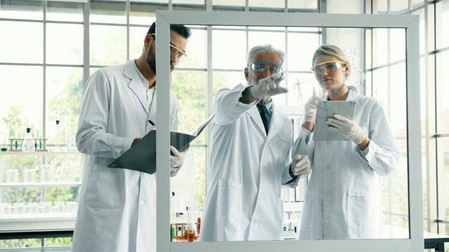 一组在实验室工作的化学家，在玻璃显示器上做笔记和书写。视频素材