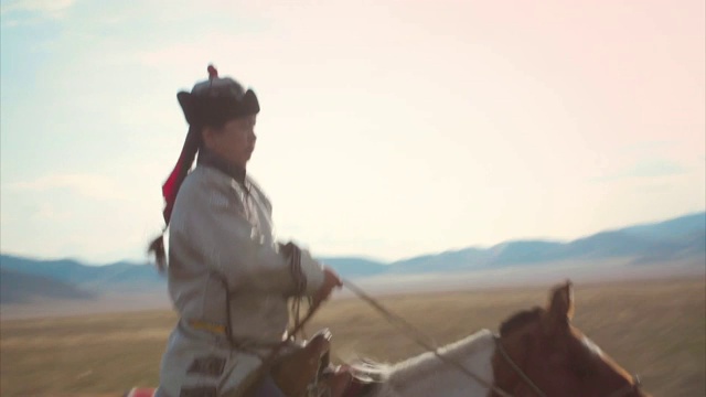 俄罗斯，一名身穿传统服饰的图瓦人骑着一匹慢跑的马。视频下载