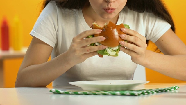 女性吃高脂肪汉堡与大胃口在快餐店，节食，肥胖视频素材