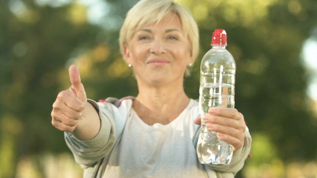 微笑的女运动员展示瓶子水和大拇指，保健，活动视频素材