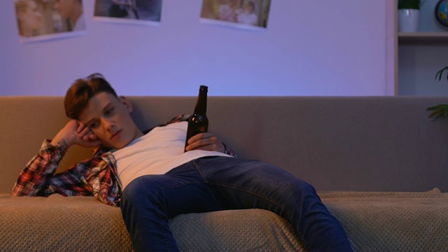 醉醺醺的少年躺在沙发上喝着啤酒，酗酒问题视频素材